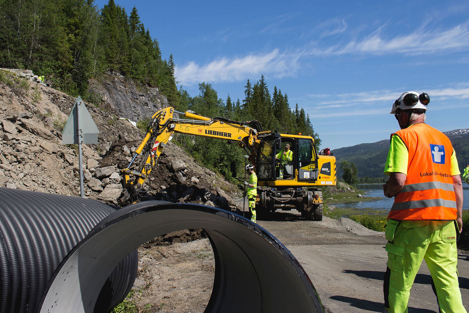 Bilde av gravemaskin med sikkerhetsvakt i forgrunnen
