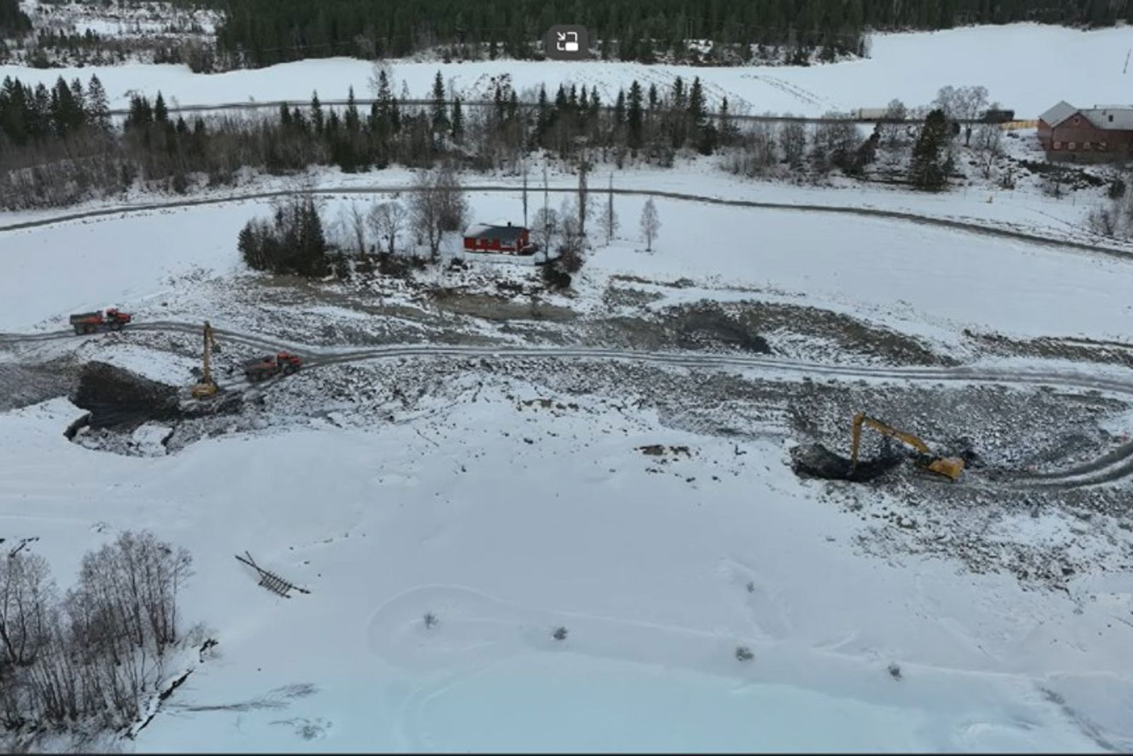 Vinterlandskap med snø over jordet + gård. Skredgropa som jevnes ut ligger under et tynt snødekke.