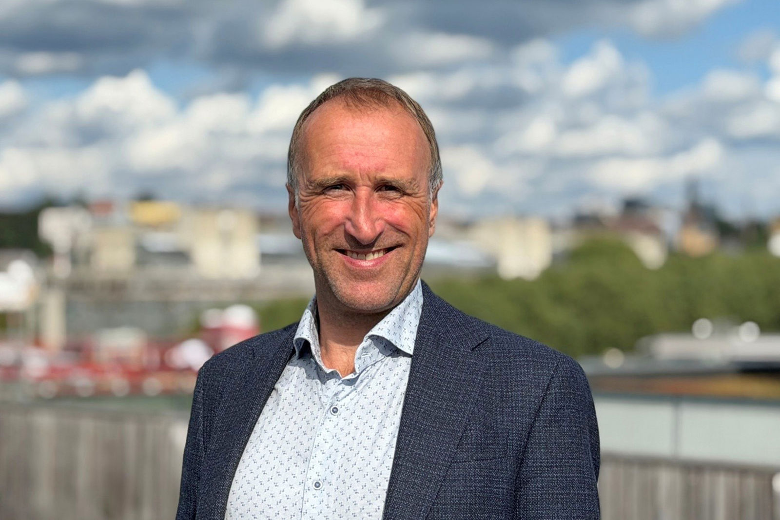 En smilende Langhelle Pedersen med en uskarp, utendørs bakgrunn.
