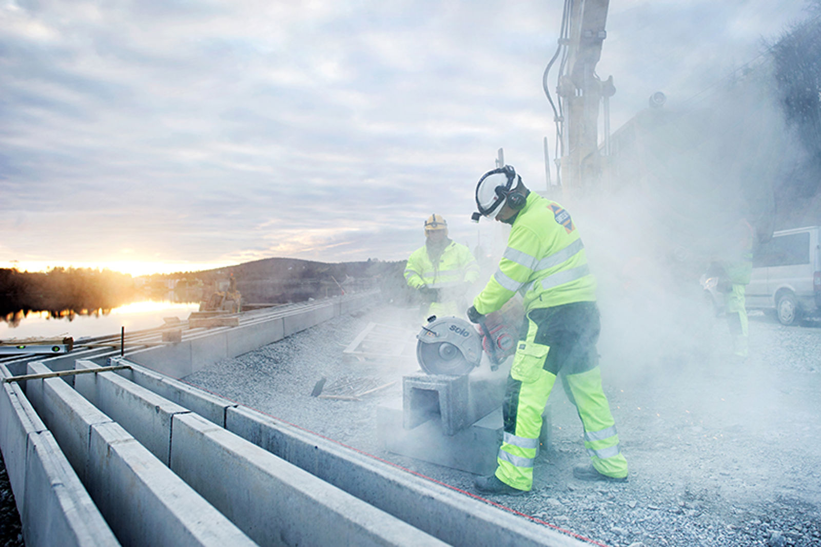 En mann i arbeidsklær bruker steinsag på en betongblokk så røykskyen står.