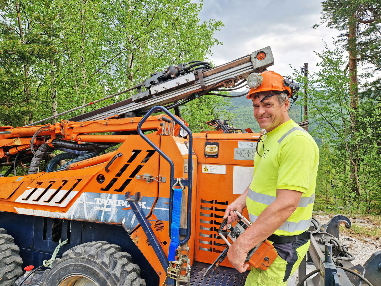 En mann i vernetøy står foran en oransje anleggsmaskin, som er en borerigg.