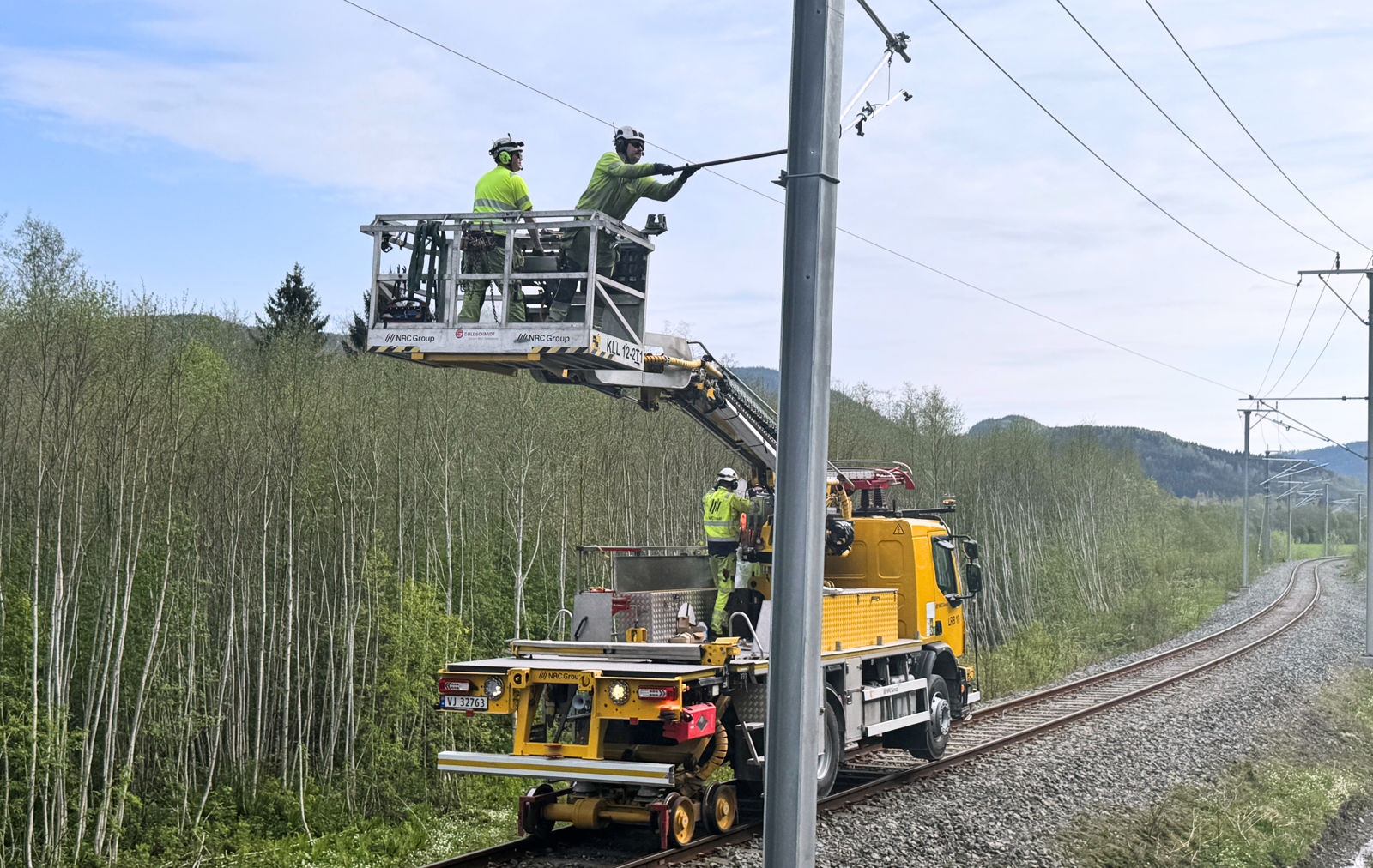 Skinnegående arbeidsmaskin med kurv, i kurven står arbeidere og jobber med KL-anlegget. 