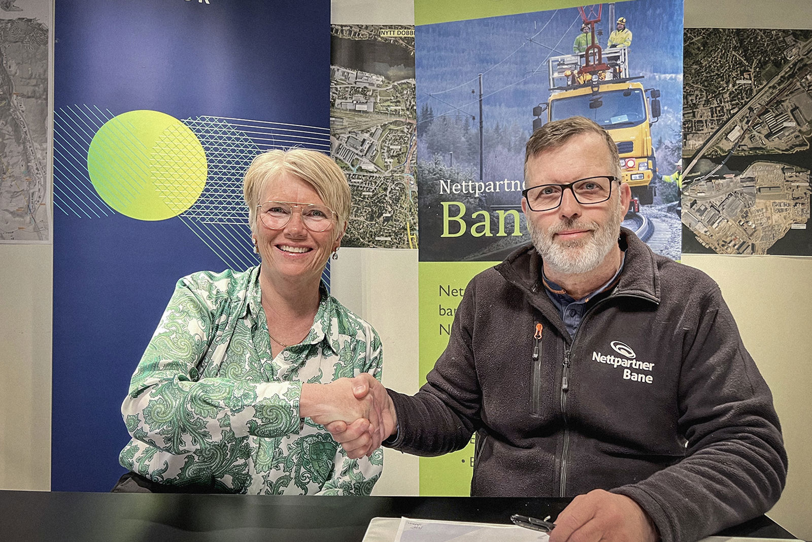 To smilende personer bak et bord utveksler håndtrykk.