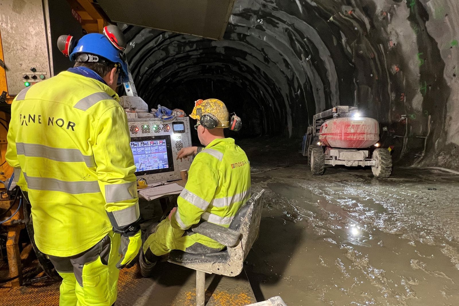 Foto som viser tunnelarbeidere ved en arbeidsrigg inne i tunnelen.