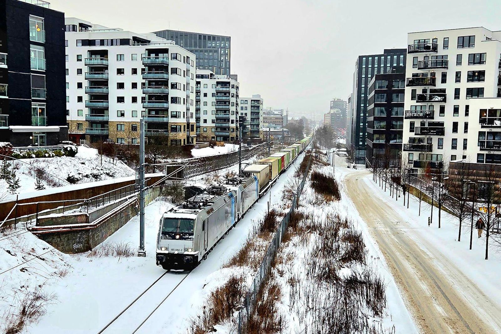 Tog med containere på rett strekning omgitt av boligblokker. Enden på toget kan knapt skimtes.