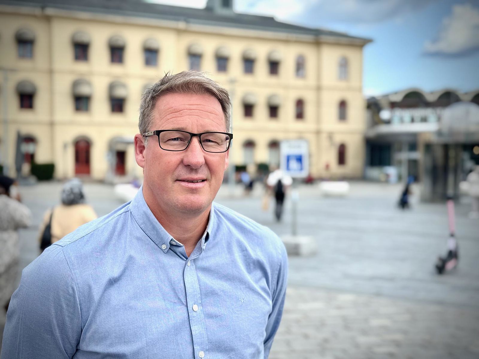 Mann står på Strømsø torg med Drammen stasjon i bakgrunn