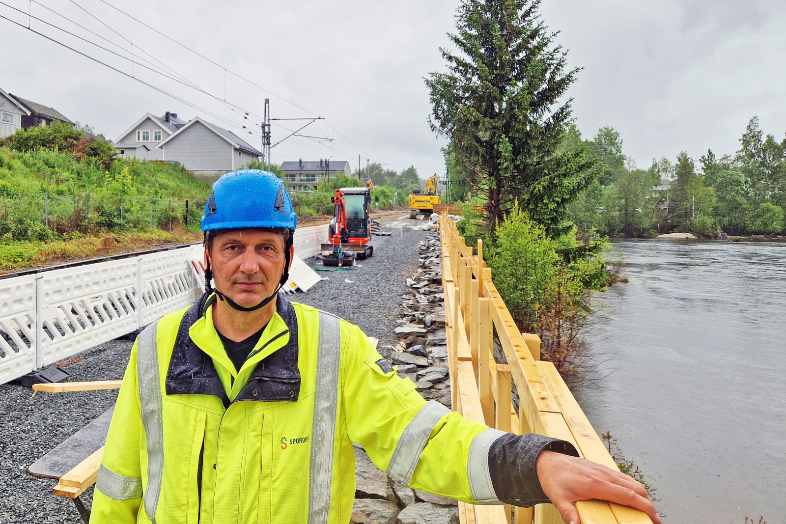 Bilde av mann i vernetøy ved et jernbanespor, som ligger rett ved en elv.
