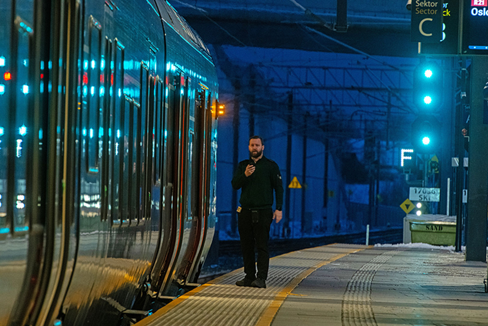 Konduktør står utenfor toget på perrongen i vintermørket.