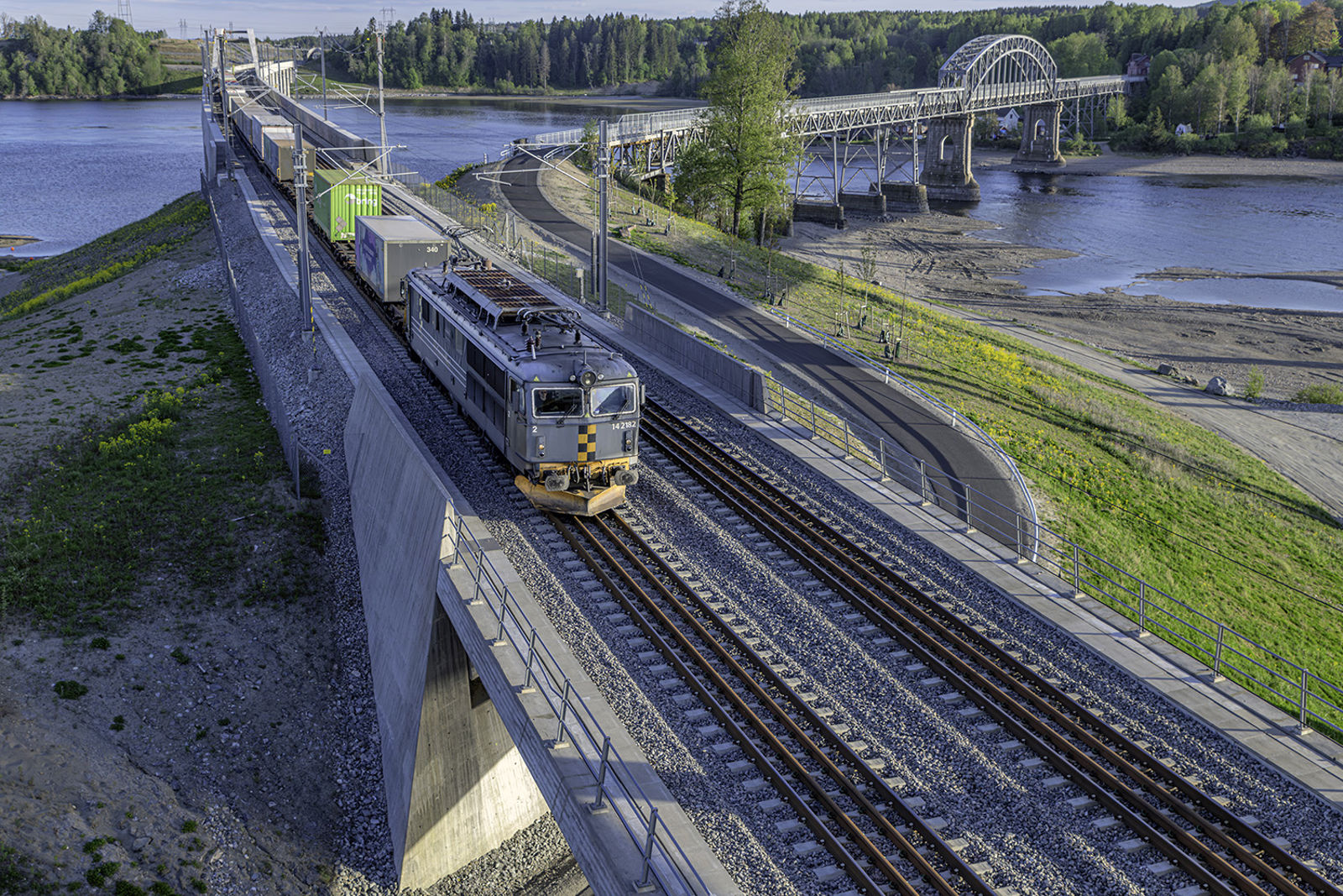 Et godstog med Vorma, gammel og ny jernbanebru i bakgrunnen.