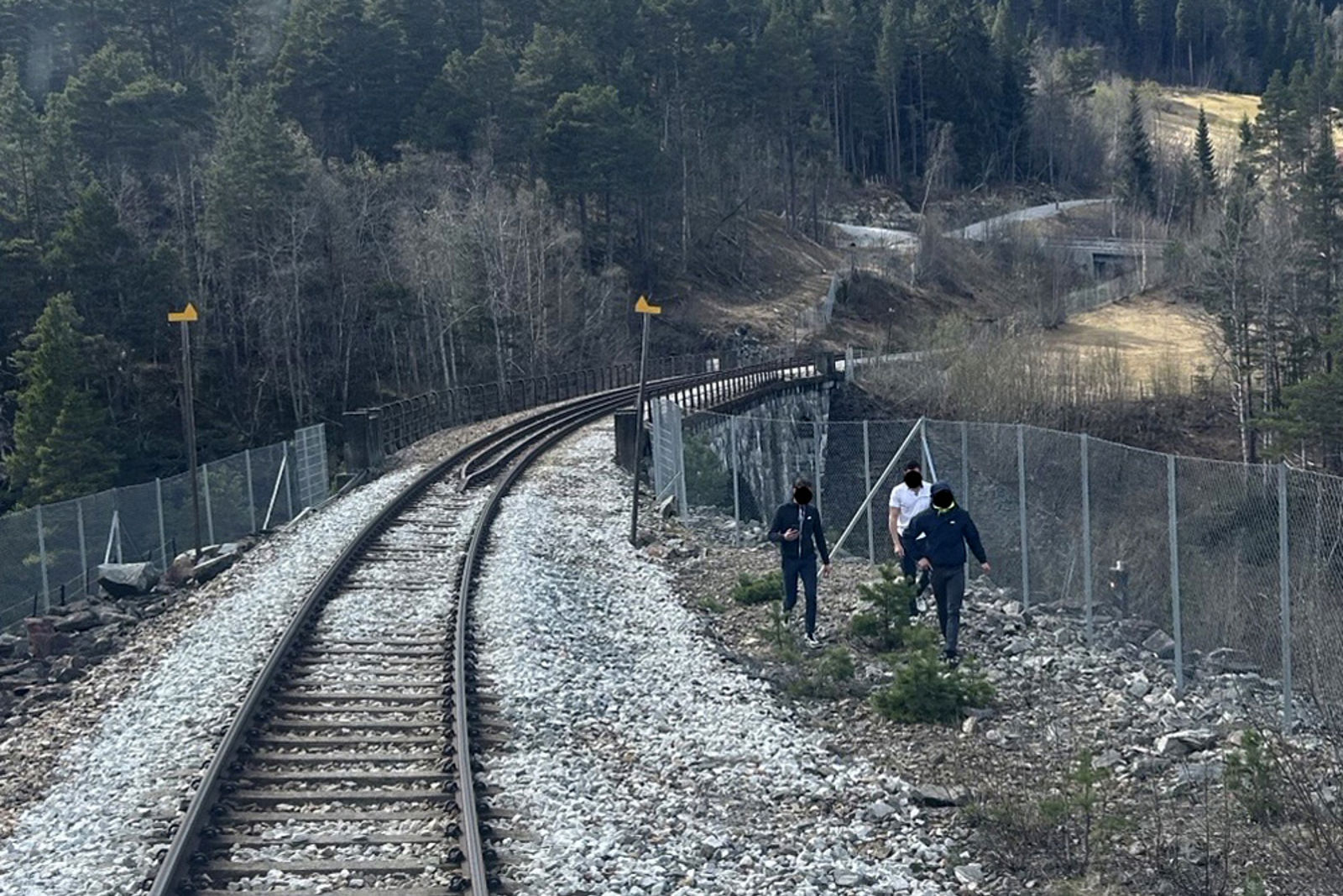 Tre personer mellom sporet og gjerdet med brua i bakgrunnen.